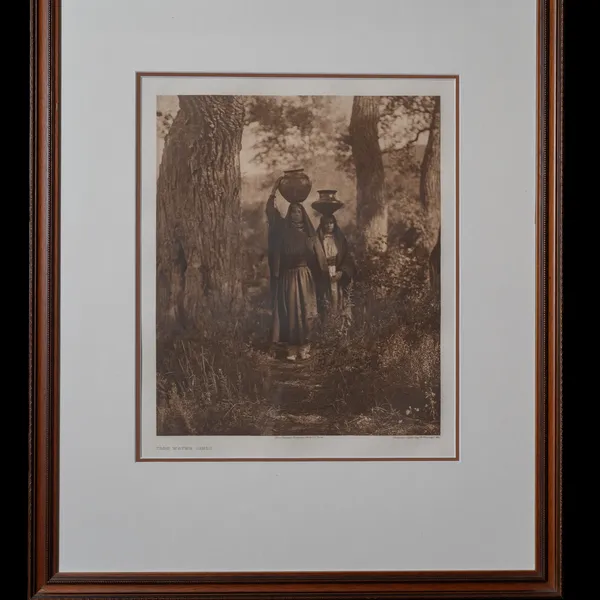 Taos Water Girls photogravure by Edward S. Curtis, 1905 - two Taos women in traditional dress carrying water jars on their heads between tall pine trees